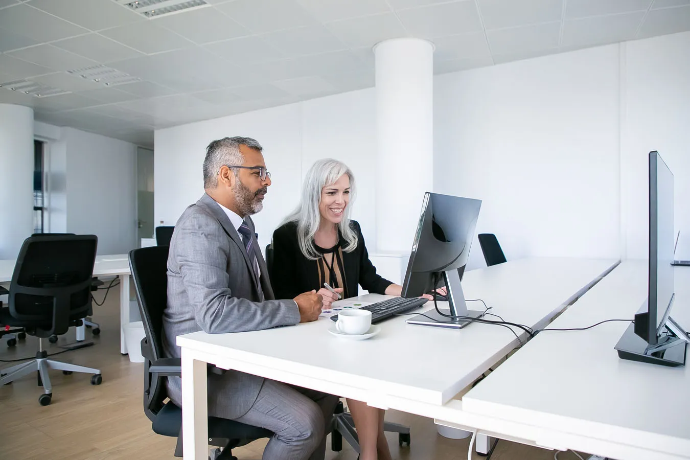 couple-cheerful-business-colleagues-watching-content-computer-monitor-smiling-laughing-while-sitting-workplace-business-communication-concept